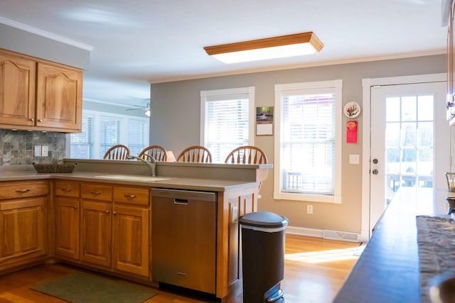 kitchen featuring a peninsula, a sink, light wood-type flooring, dishwasher, and crown molding