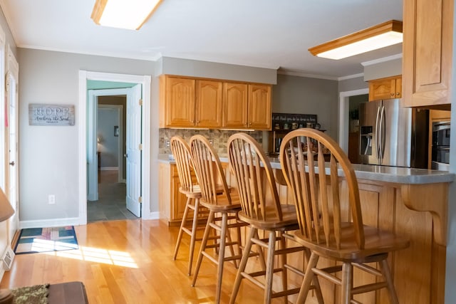 kitchen with tasteful backsplash, stainless steel fridge with ice dispenser, crown molding, light wood-style floors, and a kitchen bar