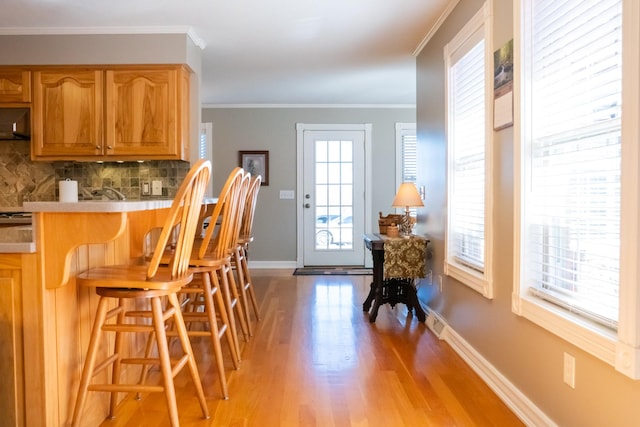 kitchen featuring ornamental molding, light wood-style floors, backsplash, and baseboards