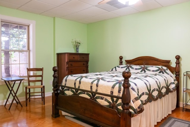 bedroom featuring a drop ceiling, visible vents, baseboards, and wood finished floors