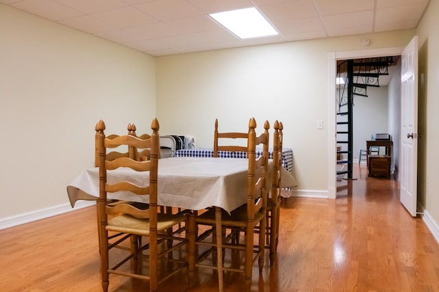 dining room featuring baseboards, a paneled ceiling, and light wood-style floors