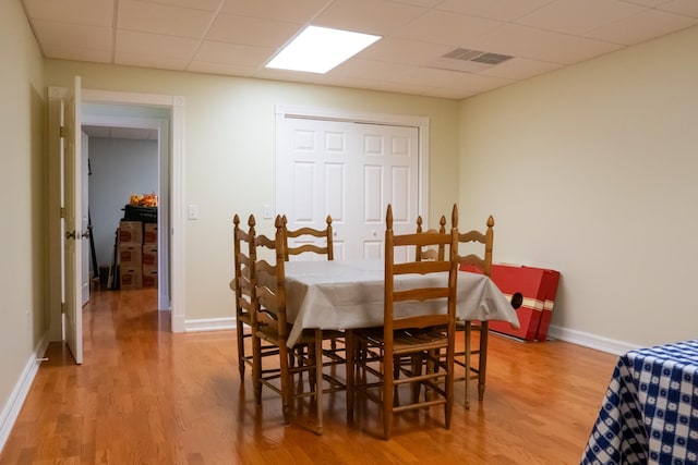 dining room with a drop ceiling, light wood-style flooring, and baseboards