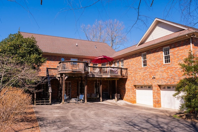 rear view of property featuring a garage, brick siding, driveway, and a wooden deck