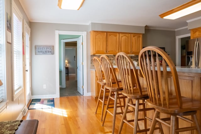 dining room featuring ornamental molding, light wood finished floors, visible vents, and baseboards