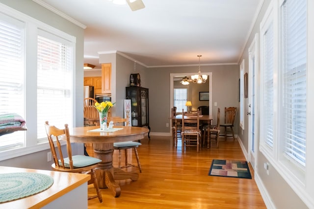 dining space with ceiling fan with notable chandelier, ornamental molding, light wood-type flooring, and baseboards