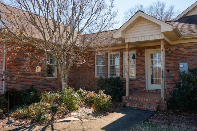 entrance to property featuring roof with shingles and brick siding