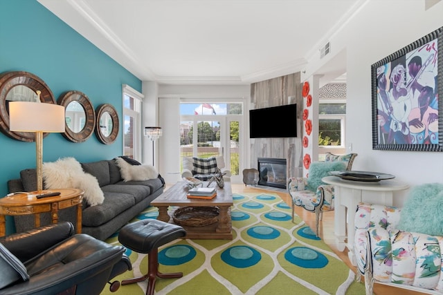 living room with a large fireplace, visible vents, crown molding, and wood finished floors