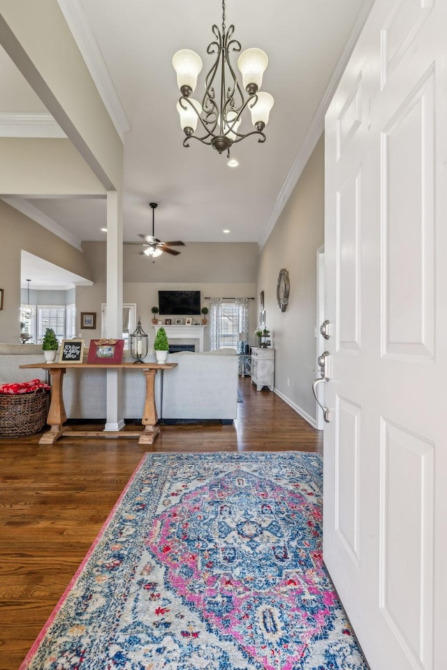 entrance foyer with ceiling fan with notable chandelier, baseboards, wood finished floors, and crown molding