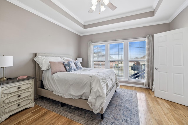 bedroom featuring light wood finished floors, a ceiling fan, a tray ceiling, and crown molding