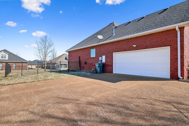 view of side of property featuring a shingled roof, brick siding, driveway, and fence