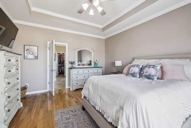 bedroom featuring a walk in closet, a raised ceiling, light wood-style flooring, and baseboards