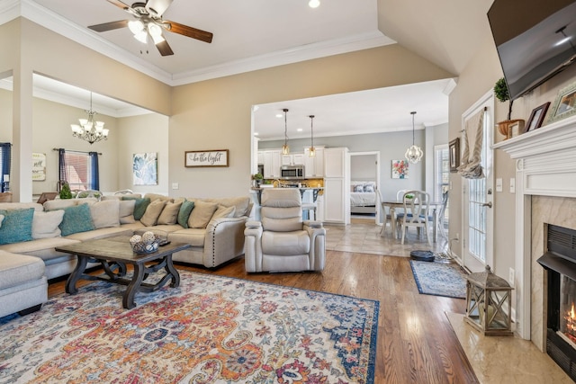 living area featuring ornamental molding, light wood finished floors, ceiling fan with notable chandelier, and a high end fireplace