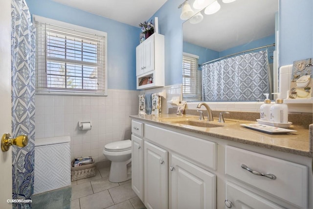 bathroom with toilet, vanity, tile walls, wainscoting, and tile patterned floors