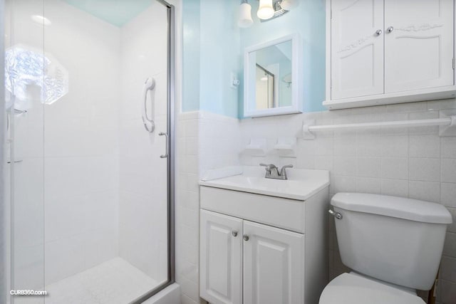 full bath featuring a stall shower, toilet, a wainscoted wall, vanity, and tile walls