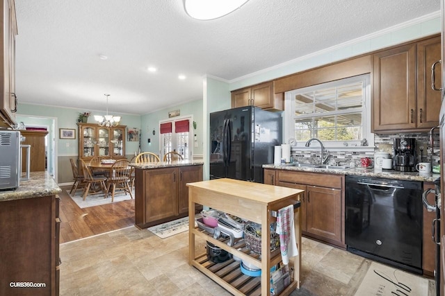 kitchen featuring light stone counters, ornamental molding, a healthy amount of sunlight, black appliances, and a sink