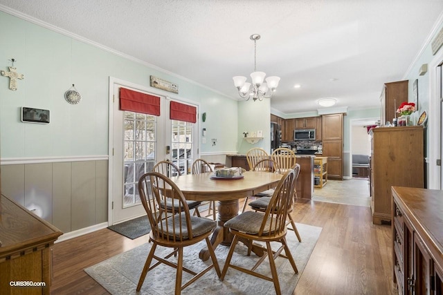 dining area with a wainscoted wall, a notable chandelier, crown molding, a textured ceiling, and light wood-type flooring