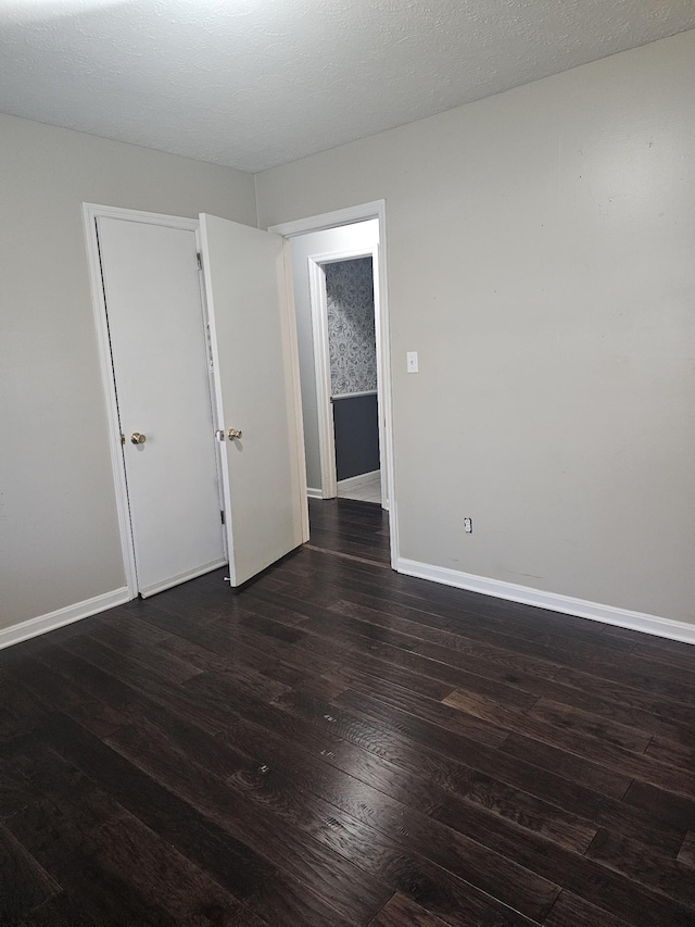 spare room featuring a textured ceiling, dark wood-type flooring, and baseboards