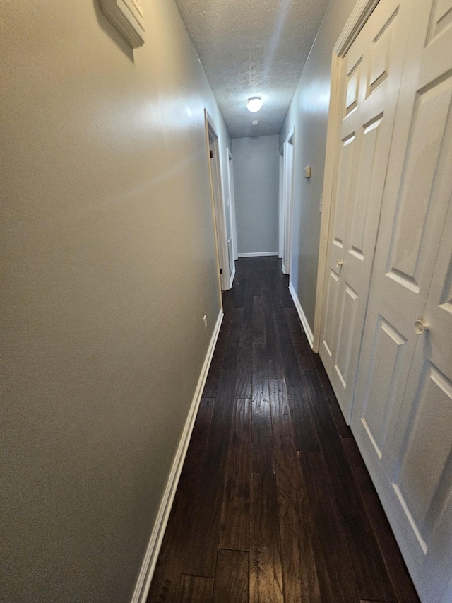 corridor featuring dark wood-style flooring, a textured ceiling, and baseboards