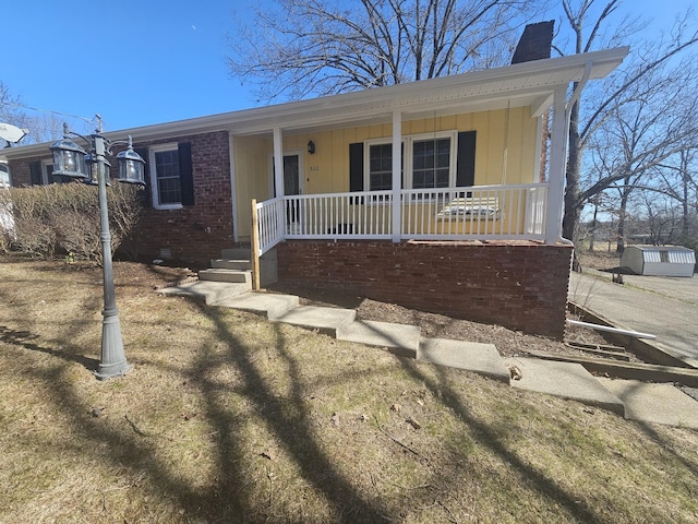 view of front of property with covered porch, crawl space, a chimney, and brick siding