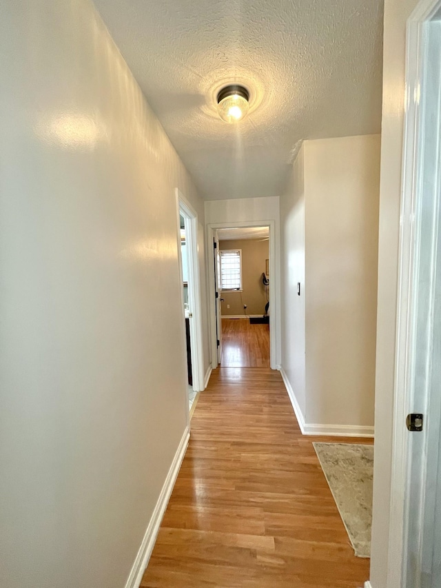 hallway featuring baseboards, a textured ceiling, and light wood finished floors