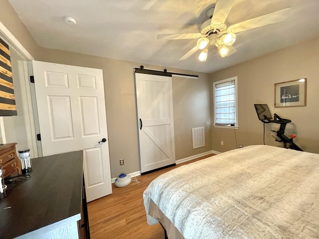 bedroom with ceiling fan, a barn door, visible vents, baseboards, and light wood-type flooring