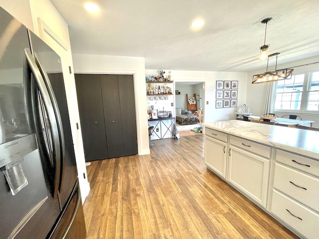 kitchen with light wood-type flooring, stainless steel fridge, white cabinetry, and decorative light fixtures