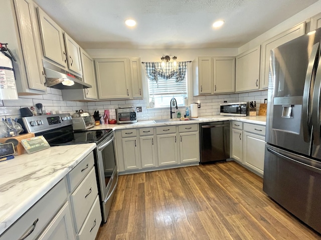 kitchen featuring tasteful backsplash, appliances with stainless steel finishes, dark wood-type flooring, under cabinet range hood, and a sink