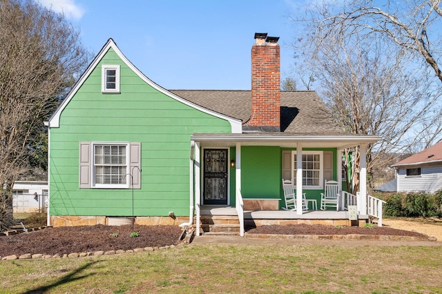 view of front facade with covered porch, roof with shingles, a chimney, and a front yard