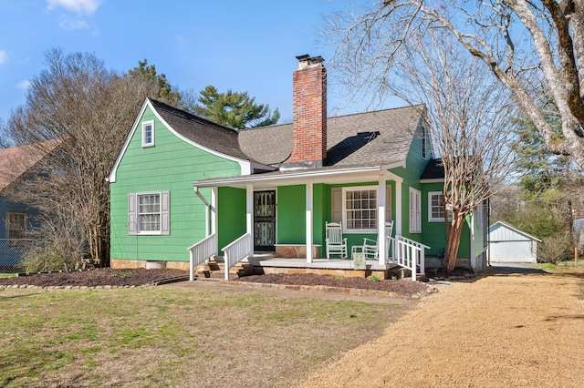 view of front of property with covered porch, a shingled roof, a chimney, and a front yard