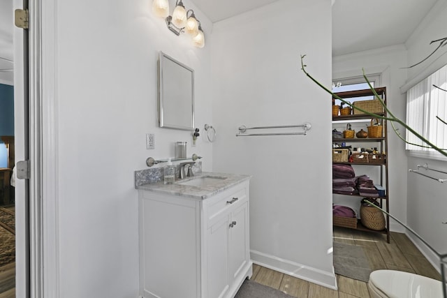 bathroom featuring toilet, ornamental molding, wood finished floors, and vanity