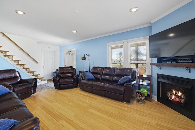 living area with a warm lit fireplace, ornamental molding, wood finished floors, and recessed lighting
