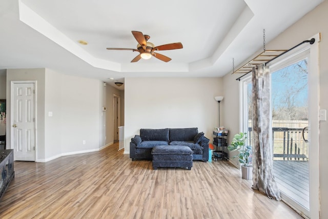 living area featuring a raised ceiling, ceiling fan, baseboards, and wood finished floors