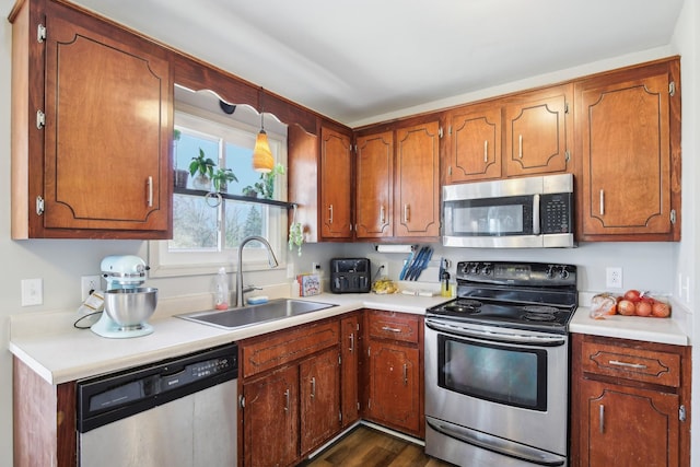 kitchen featuring stainless steel appliances, light countertops, brown cabinetry, and a sink