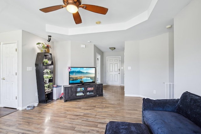 living area featuring a raised ceiling, wood finished floors, a ceiling fan, and baseboards