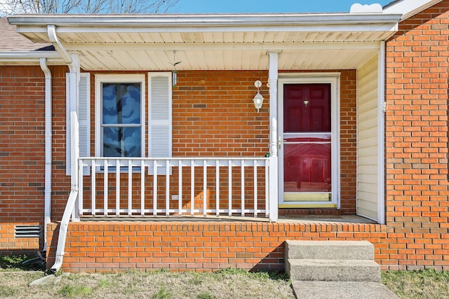 view of exterior entry featuring crawl space, a porch, and brick siding