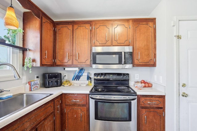 kitchen with appliances with stainless steel finishes, brown cabinets, light countertops, and a sink