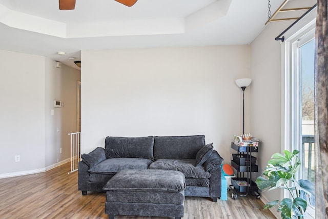 living area featuring wood finished floors, a raised ceiling, a ceiling fan, and baseboards