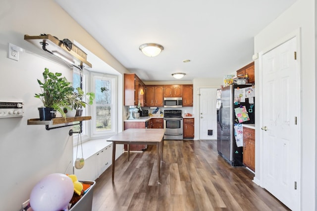 kitchen featuring brown cabinets, dark wood-type flooring, stainless steel appliances, light countertops, and a sink