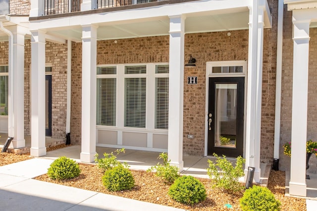 view of exterior entry featuring a porch and brick siding