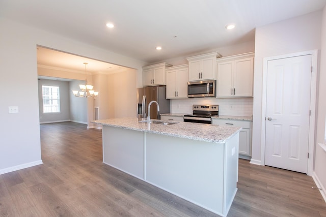 kitchen featuring appliances with stainless steel finishes, wood finished floors, a center island with sink, and tasteful backsplash