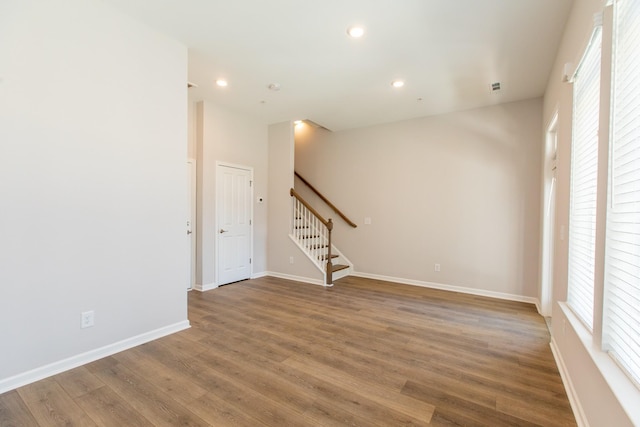 unfurnished room with stairs, baseboards, wood finished floors, and a healthy amount of sunlight