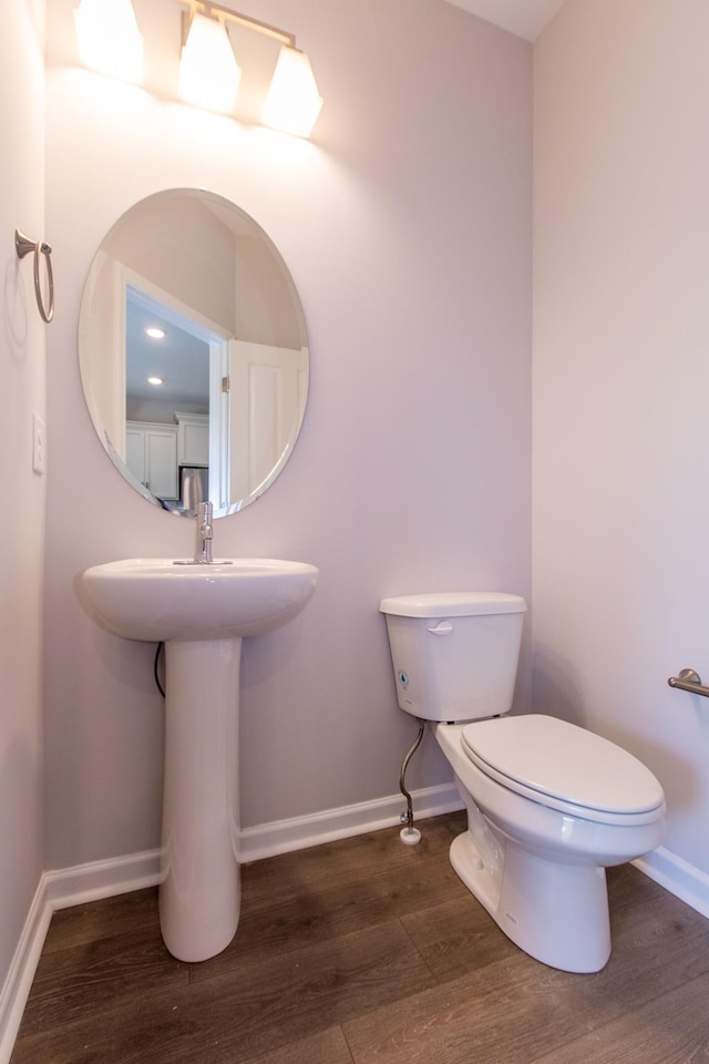 half bathroom featuring wood finished floors, toilet, and baseboards