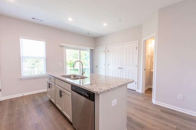 kitchen featuring visible vents, light wood-style flooring, stainless steel dishwasher, a kitchen island with sink, and a sink