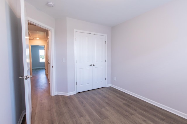 unfurnished bedroom with dark wood-style flooring, a closet, attic access, and baseboards