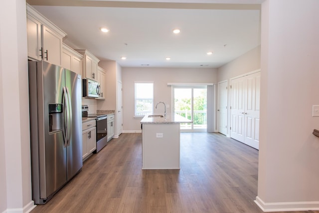 kitchen with a center island with sink, stainless steel appliances, recessed lighting, a sink, and wood finished floors