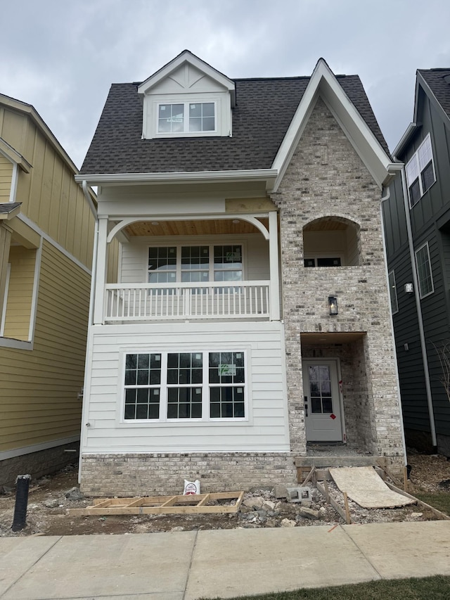 view of front of house featuring brick siding, a shingled roof, and a balcony