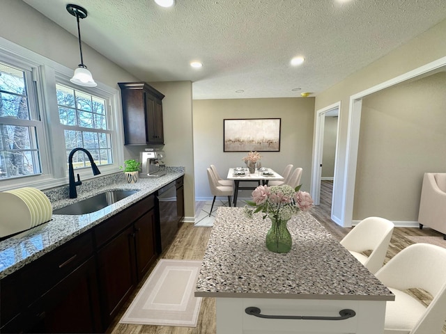 kitchen with dishwasher, light stone counters, dark brown cabinets, light wood-style floors, and a sink