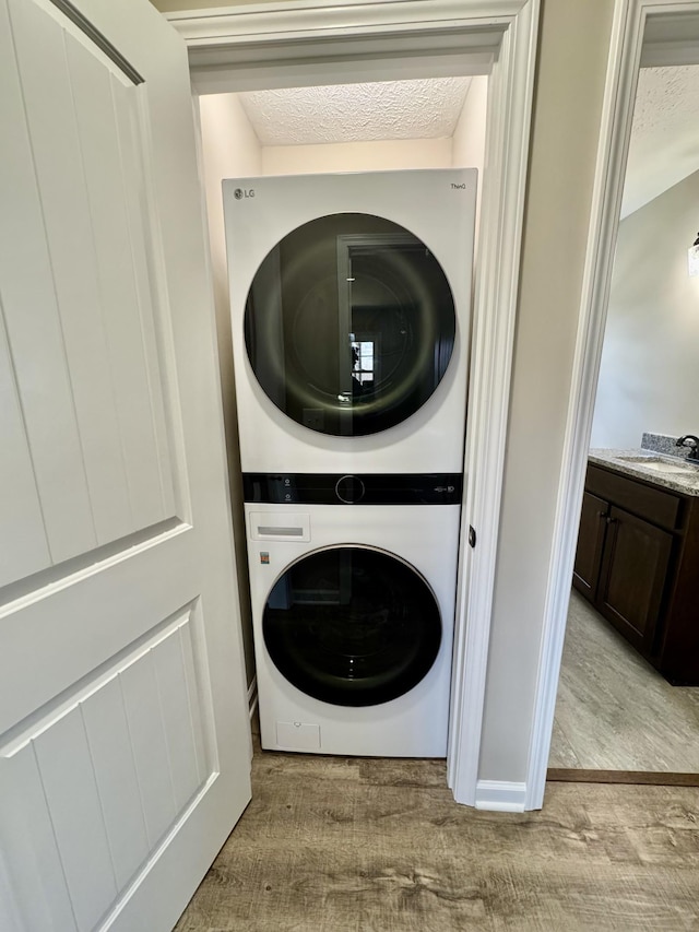 laundry area featuring light wood finished floors, stacked washer / dryer, a sink, a textured ceiling, and laundry area