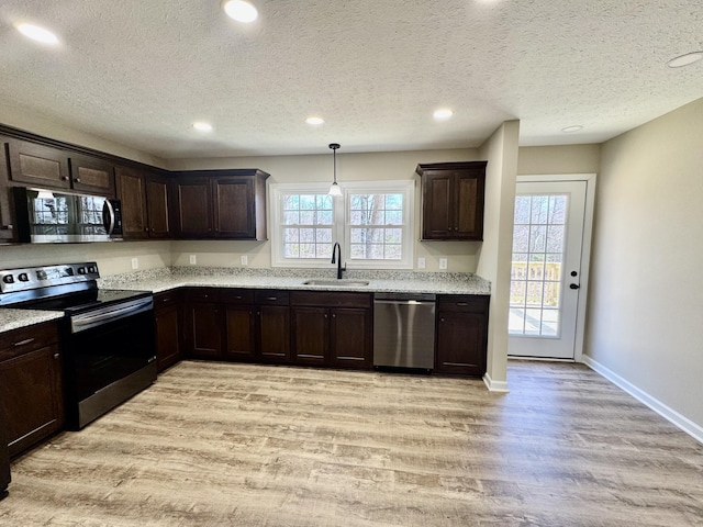 kitchen featuring light wood-type flooring, dark brown cabinetry, appliances with stainless steel finishes, and a sink