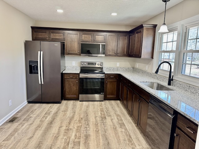 kitchen featuring dark brown cabinetry, stainless steel appliances, a sink, and light wood finished floors